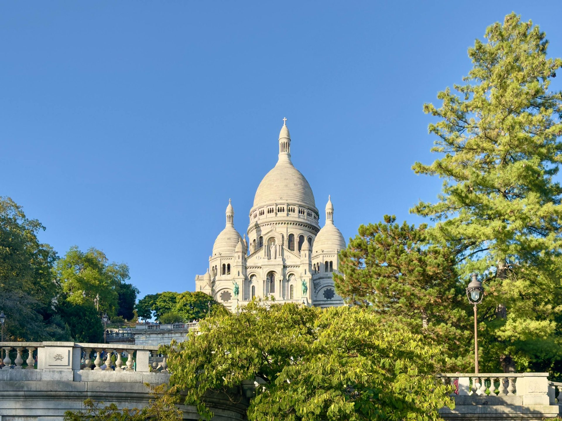 The Sacre Coeur Basilica in Paris towers amidst greenery under a clear blue sky.